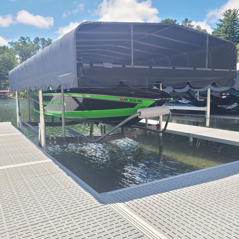 Green jet ski on a lift under a canopy at a dock on calm water.