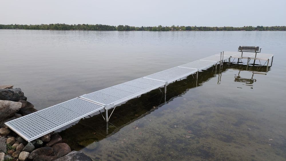 Aluminum dock extending over calm lake water with a seating area at the end.