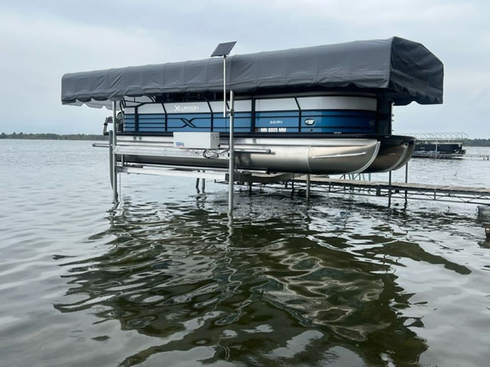 Pontoon boat with covered canopy docked on a lake, surrounded by calm water.