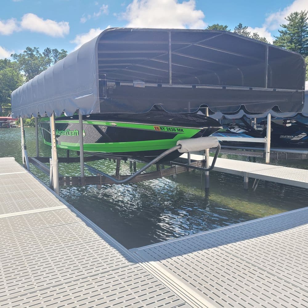 Green speedboat under a covered dock on a calm lake, surrounded by jet skis and trees.