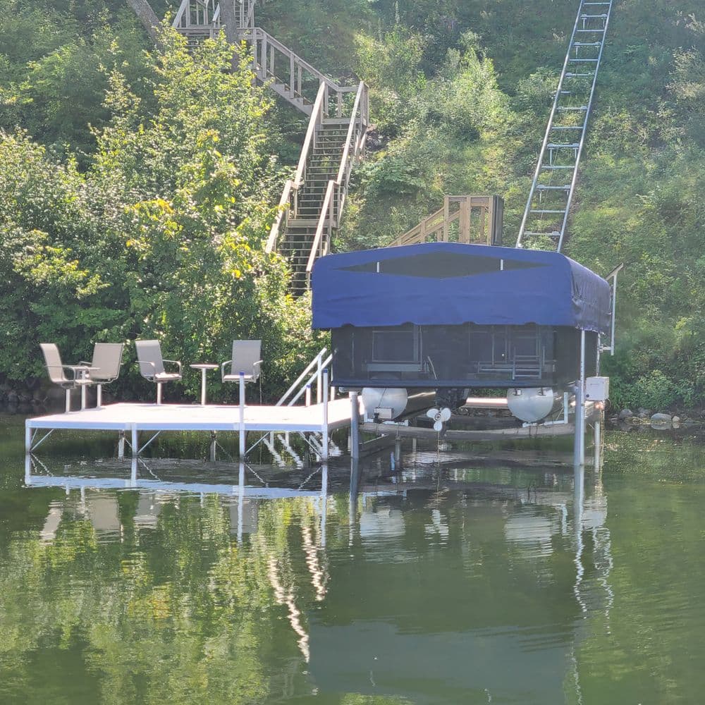 Dock and boat lift on calm water, surrounded by greenery and stairs in the background.